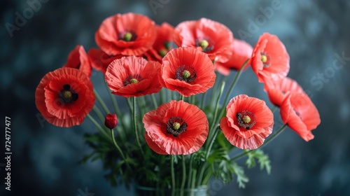  a vase filled with red flowers sitting on top of a wooden table next to a blue wall and a black wall behind the vase is a bunch of red poppies. © Shanti