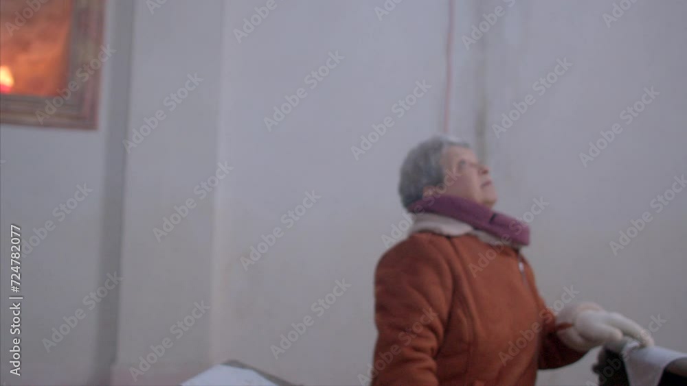 Elderly couple visits local Catholic church indoors, emphasizing role of religion in people's lives. A pensioner man takes a photo on a smartphone. Candles are burning at Christmas. Elderly couple visits local Catholic church indoors, emphasizing role of religion in people's lives. A pensioner man takes a photo on a smartphone. Candles are burning at Christmas.