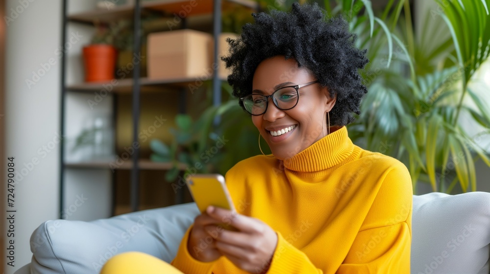 A smiling, happy middle-aged black business woman in the office is sitting on the couch and looking at the phone she is holding in her hands A smiling, happy middle-aged black business woman in the office is sitting on the couch and looking at the phone she is holding in her hands