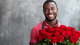 Cute smiling African American male flower seller with blue eyes, wearing an apron with a large bouquet of red roses on a gray background. Gardening, floristry and holidays concept