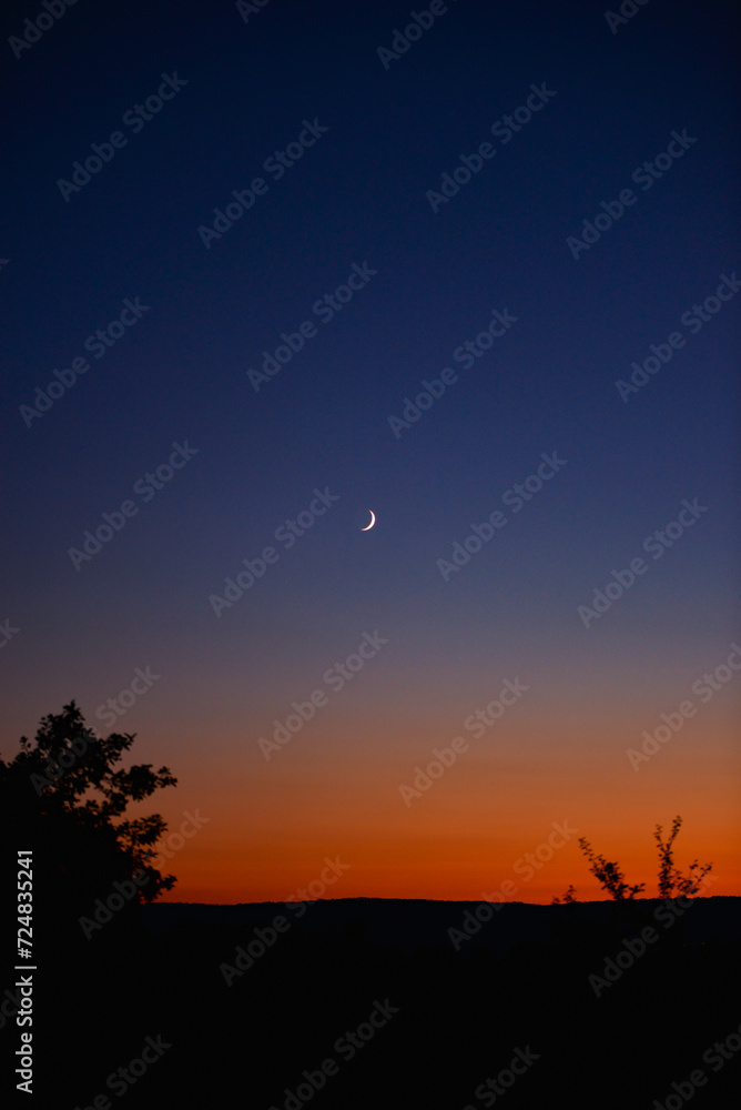 Young crescent moon on a clear sky at the end of the day in the summer
