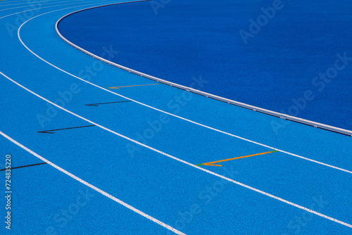 Blue stadium track lanes with white stripes, an empty background suitable for copy space, represent the concept of physical sports and running, symbolizing commitment and pathways towards goals