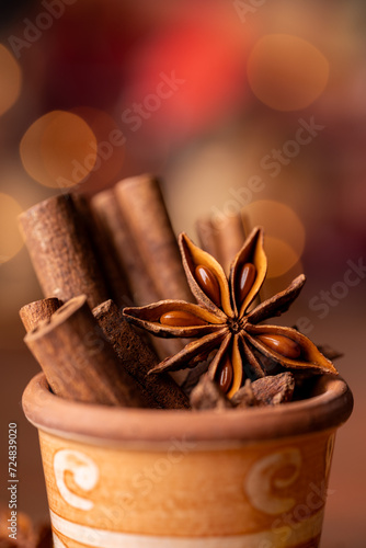 In the foreground, in a colored earthenware jar, some cinnamon sticks and an anise star, lights on a bokeh background. Still life