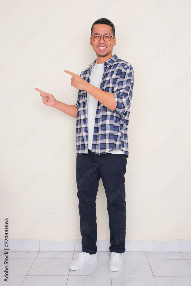 Full body portrait of a man smiling with both hands pointing to the right side Full body portrait of a man smiling with both hands pointing to the right side