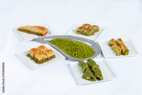 Top view of baklava varieties on white plates and milled pistachio isolated on white background.
