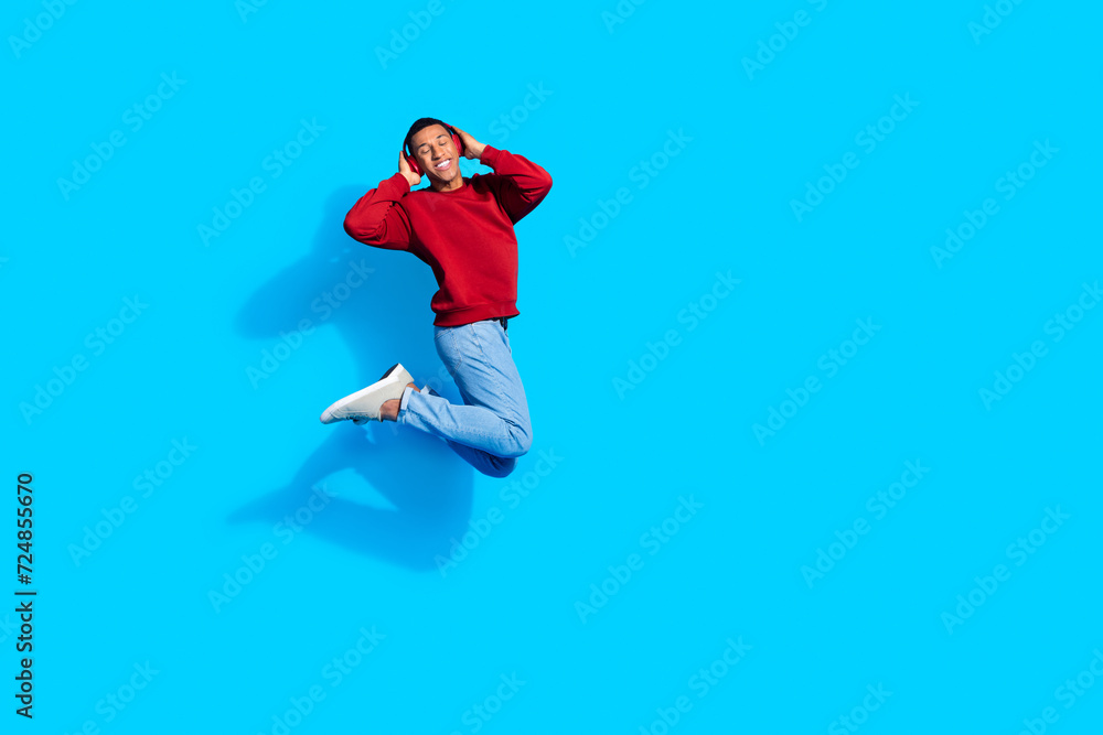 Photo of joyful positive man wear red trendy sweatshirt listen music wireless headphones empty space isolated on blue color background Photo of joyful positive man wear red trendy sweatshirt listen music wireless headphones empty space isolated on blue color background