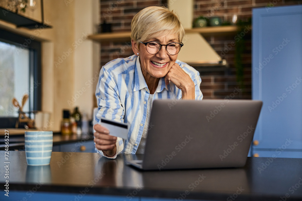 A smiling senior woman using a laptop, holding a credit card, and buying something online. A smiling senior woman using a laptop, holding a credit card, and buying something online.