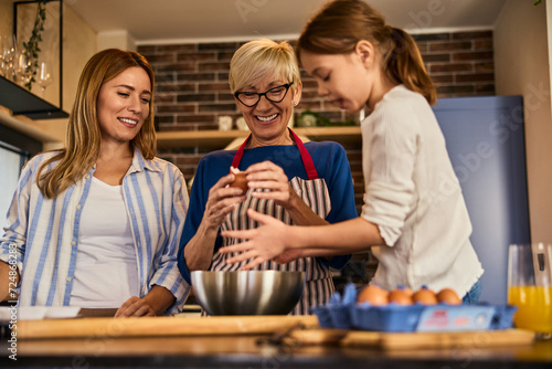 Three generations are cooking in the kitchen, enjoying each other, and a little girl is helping her mother and grandma.