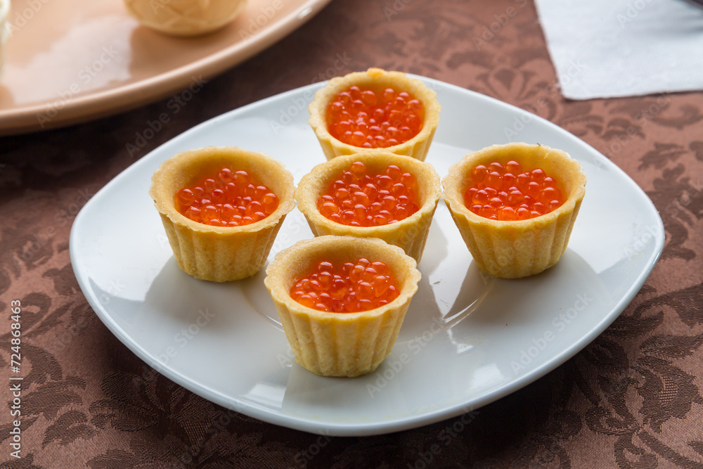 Red caviar in tartlets on a plate on a brown tablecloth. Horizontal Red caviar in tartlets on a plate on a brown tablecloth. Horizontal