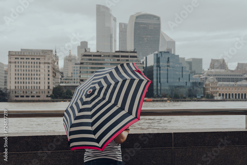 Unidentifiable woman with umbrella standing by the River Thames in London, UK. photo