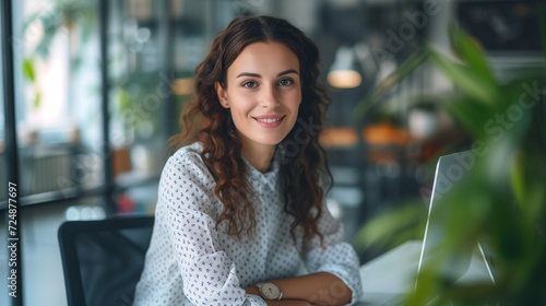 Smiling young woman with curly hair at her computer in a modern office with greenery photo