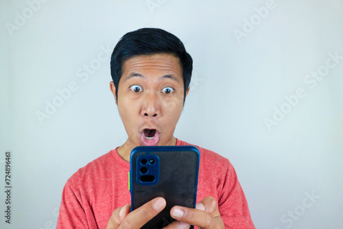 funny facial expression of asian man shocked and shocked holding and looking at phone screen photo
