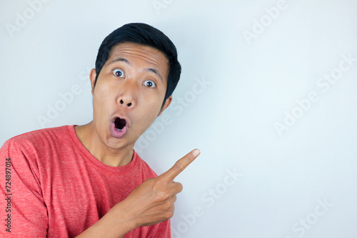 funny facial expression of asian man shocked and surprised while pointing at left side photo