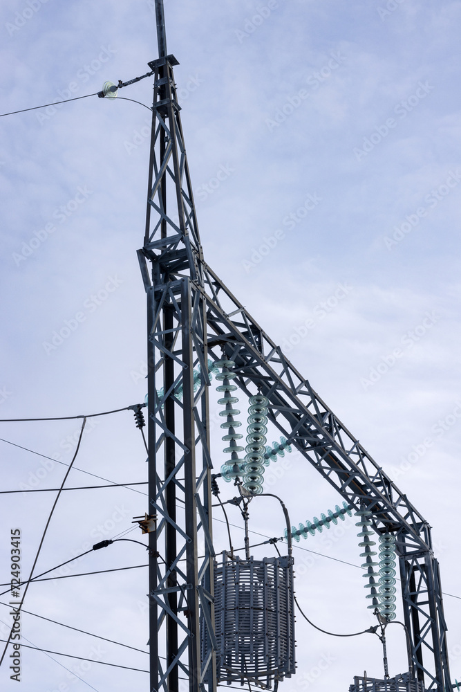 Supports and truss of a power line with insulators and wires, vertically against a blue sky background.