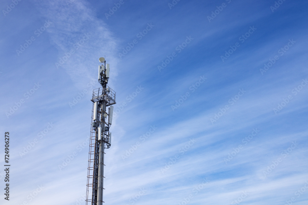 A tower telecommunications tower with antennas, against a background of blue sky with light clouds A tower telecommunications tower with antennas, against a background of blue sky with light clouds