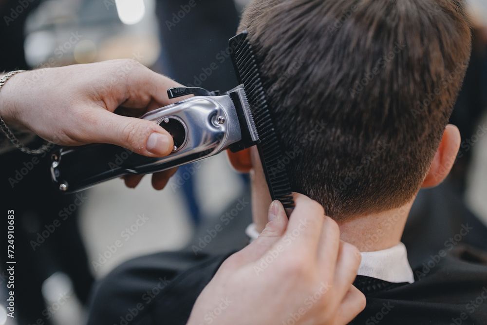 Fototapeta premium Closeup master barber hairdresser does hairstyle with hair clipper and comb. Concept banner Barbershop for man