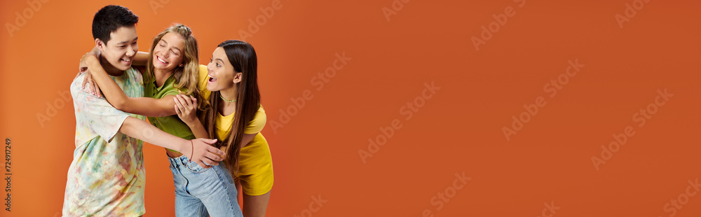 jolly diverse teens in bright attires hugging each other on orange backdrop, friendship day, banner jolly diverse teens in bright attires hugging each other on orange backdrop, friendship day, banner