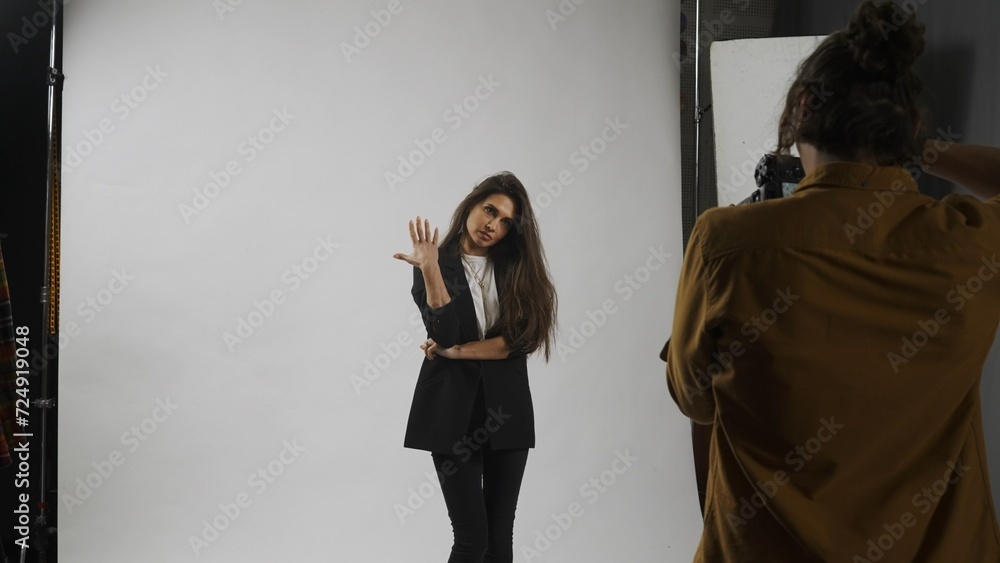 Fototapeta premium Backstage of model and professional team in the studio. Full length of attractive model in suit posing, photographer taking pics, cool expression.