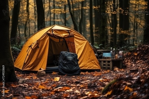 A tent stands among the trees in a peaceful woods, with a backpack resting on the ground nearby, Tourist's survival kit and camping tent in autumn forest, AI Generated © Iftikhar alam