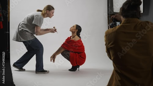 Model and production team in the studio. Woman model posing, photographer asks makeup artist fix hair and makeup on set. photo