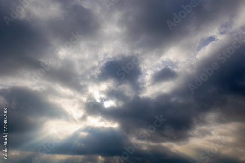 Ray of sun or sunbeam shining through the cloudy cumulus clouds floating in the skies, White grey fluffy clouds on sky before raining, Nature pattern background.