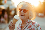 Cheerful elderly woman eating ice cream outdoors on sunny summer day. Senior lady having a dessert in outdoor cafe.