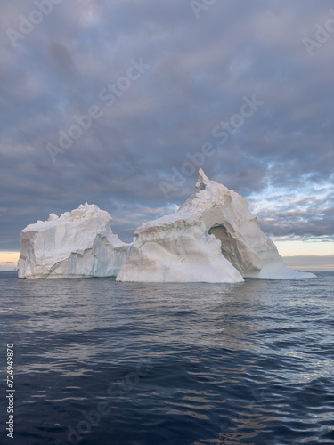 A huge high breakaway glacier drifts in the southern ocean off the coast of Antarctica at sunset  the Antarctic Peninsula  the Southern Arctic Circle  azure water  cloudy weather