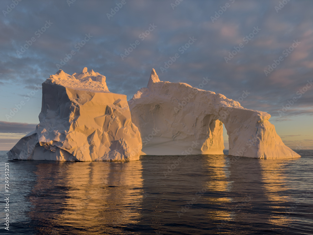 A huge high breakaway glacier drifts in the southern ocean off the coast of Antarctica at sunset, the Antarctic Peninsula, the Southern Arctic Circle, azure water, cloudy weather