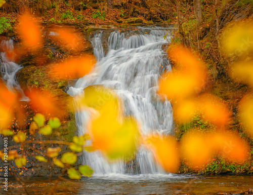 close up view to cascade of waterfall through autumn leaves © sergejson