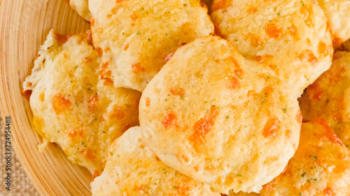 Cheese biscuits with butter and garlic seasoning topping close-up on a wooden plate, flat lay