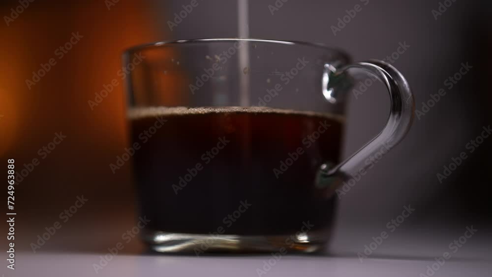 Closeup side view of pouring milk into coffee drink at dark room on blurred light on background. Pouring milk in transparent glass coffee cup. Slow motion shot of cream splash in coffee. Closeup side view of pouring milk into coffee drink at dark room on blurred light on background. Pouring milk in transparent glass coffee cup. Slow motion shot of cream splash in coffee.
