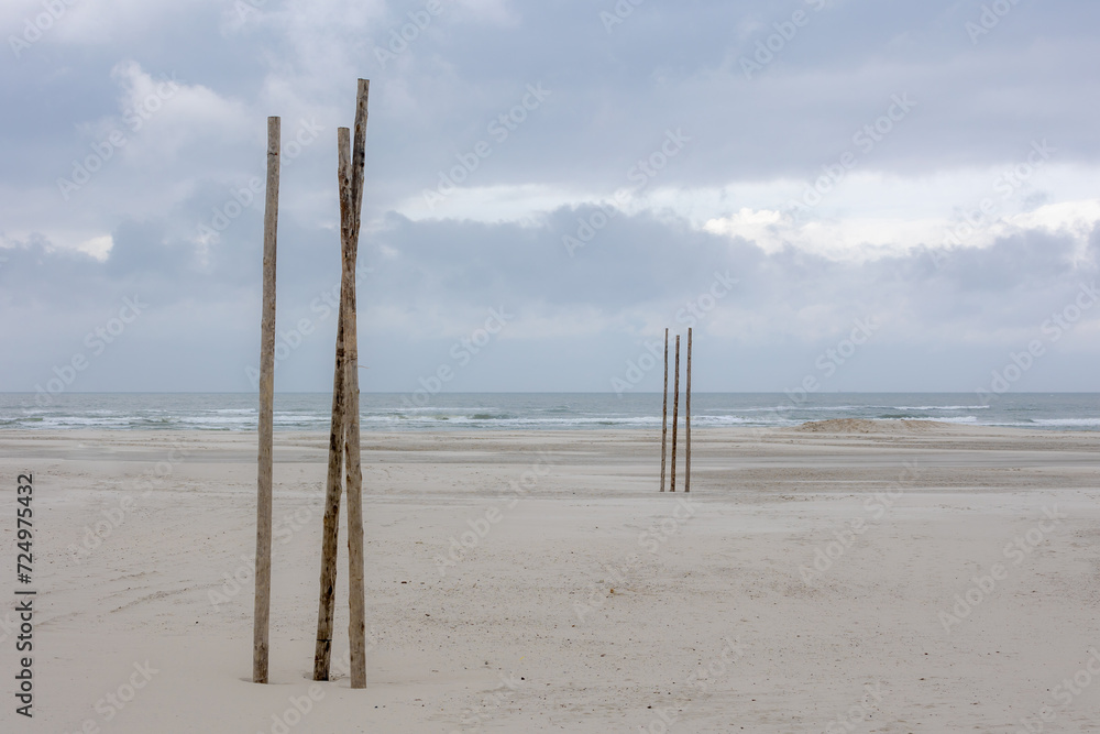 Wide and long sand beach under white grey cloudy sky, Wooden pole along the seashore of the Dutch Wadden Sea island Terschelling, A municipality and an island in the northern, Friesland, Netherlands.