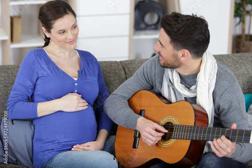 beautiful pregnant woman and handsome husband playing acoustic guitar