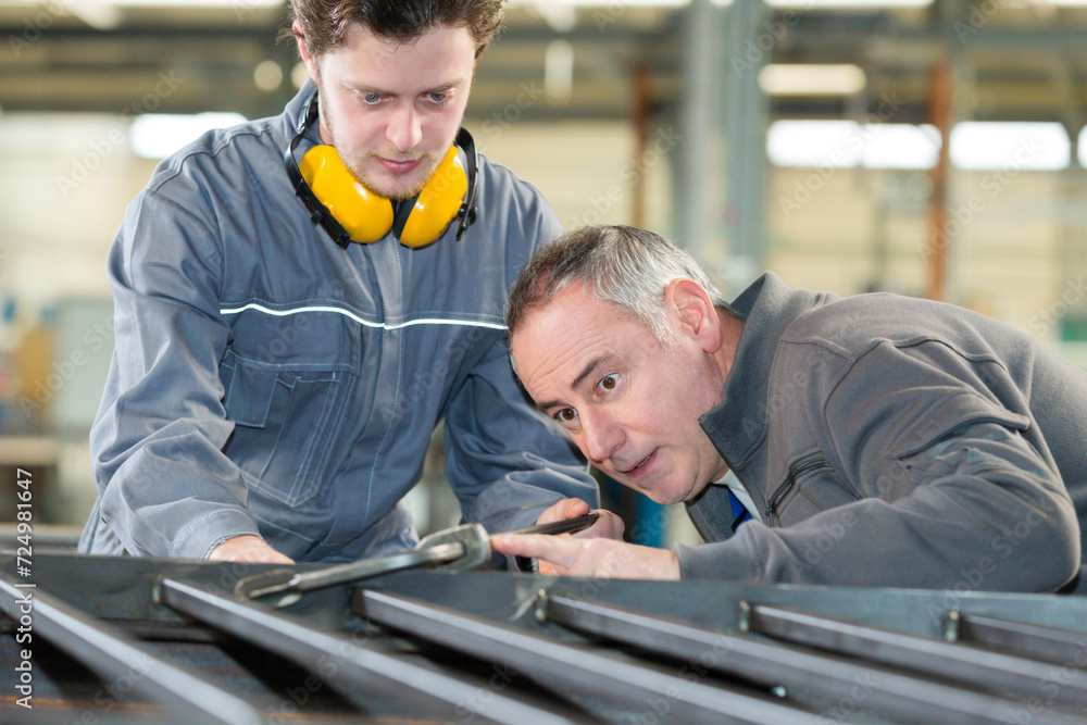 Fototapeta premium two industrial workers inspecting work piece standing on the fac
