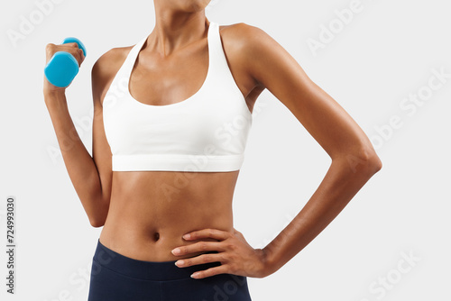 Latin American woman lifts dumbbells, young female athlete doing fitness workout, engaged in physical activity to improve health and fitness. Sportswoman do training, isolated over gray background
