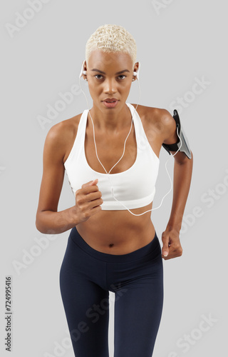 Fitness workout, running woman with earphones of mobile phone on arm band, african latin american female athlete in sportswear, exercising in gym or jogging, isolated on grey background