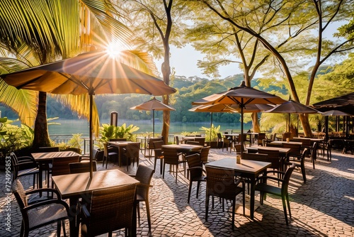 Outdoor restaurant patio with empty tables and umbrellas by a tranquil lake surrounded by greenery  basking in the warm morning sunlight.