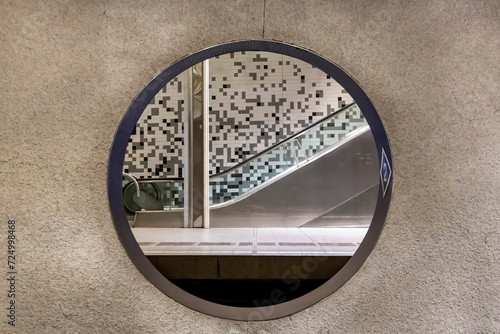 Rotterdam, The Netherlands; View through a round opening in out of focus concrete wall of the Wilhelminaplein subway station with platform and escalator on other side