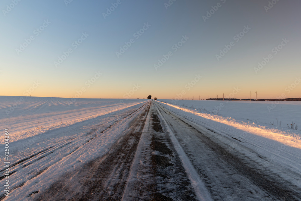 slippery and dangerous road covered with snow and ice at sunset