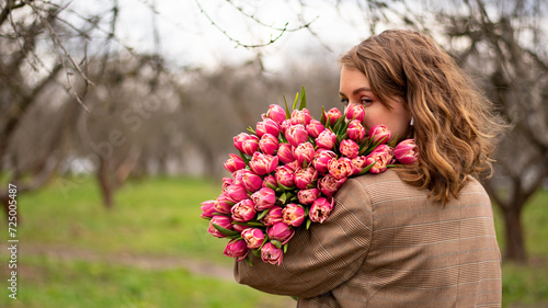 Blonde girl in beige jacket with a large bouquet of pink tulips