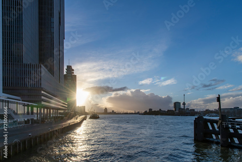 Panoramic view over the Maas river in Rotterdam, The Netherlands with high rise buildings on Holland Amerika Kade on the quay side during sunset with blue sky and clouds