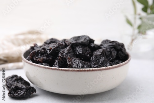 Bowl with sweet dried prunes on light table, closeup