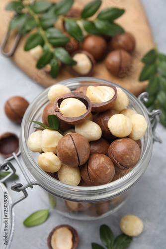 Tasty Macadamia nuts in jar on light grey table, closeup
