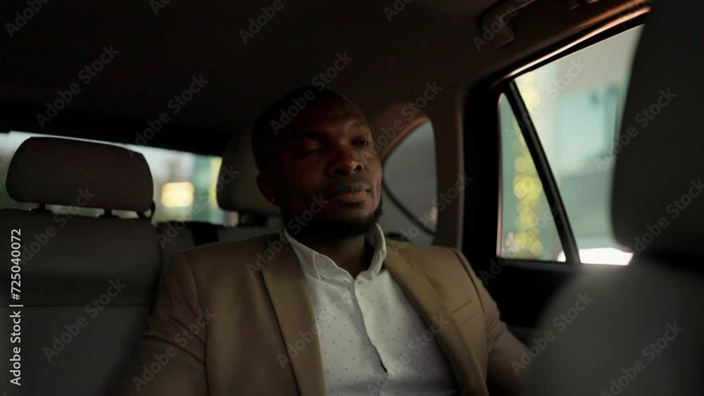 A happy and confident man with Black skin and a beard in a brown suit rides in a modern car after a business meeting and looks out the window A happy and confident man with Black skin and a beard in a brown suit rides in a modern car after a business meeting and looks out the window