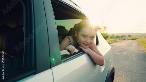 child girl face looks smiling from car out window, summer vacation mood, car driving time, summer time, summer trip with family by car, schoolgirl, girl sitting back seat car with her hand out window © DREAM INSPIRATION