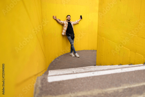 fabulous hispanic man leaning on a colorful yellow wall happy for his achievements