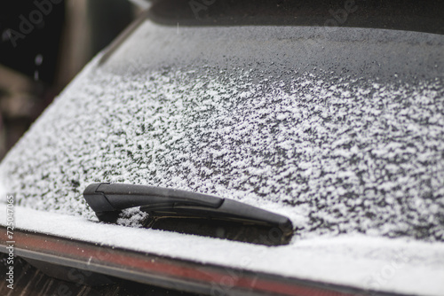Close-up shot of a car's windscreen wiper covered in snow. Fresh snow lies on the car window.