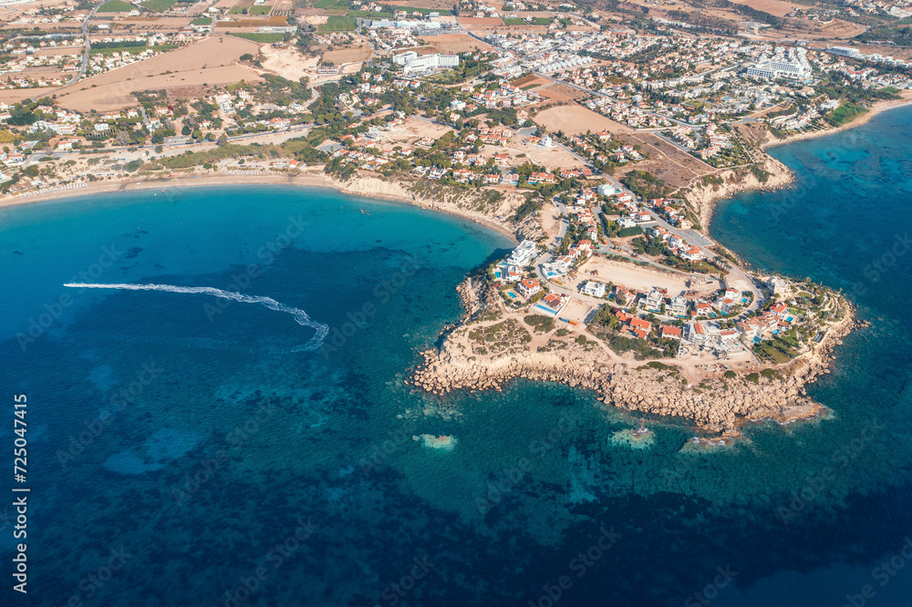 Fototapeta premium Aerial top down view of picturesque village nestled by Cyprus coastline, with azure waters and boats dotting seascape.