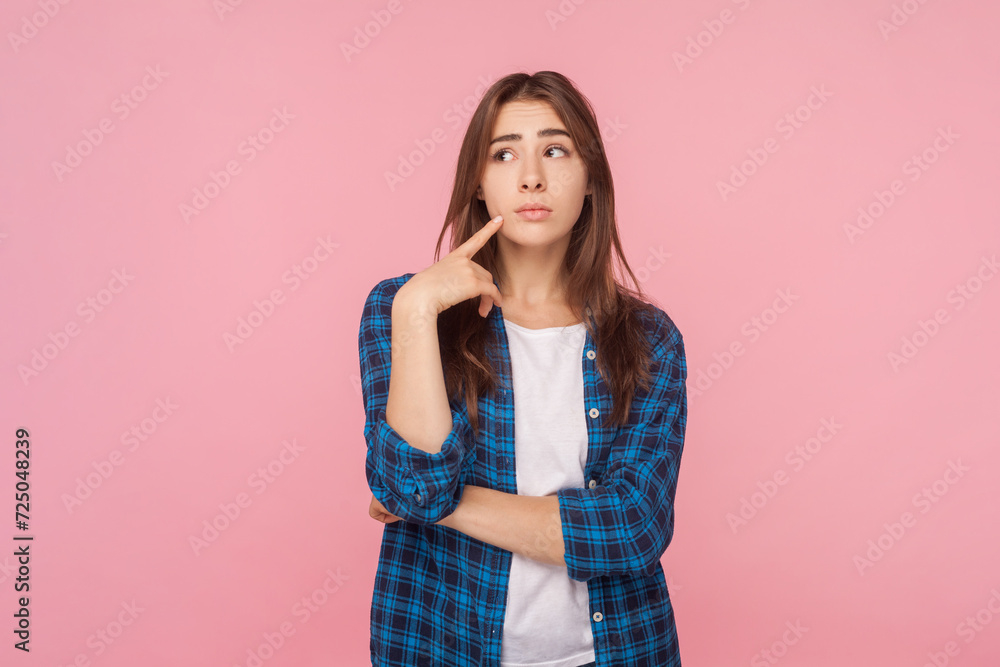 Portrait of pensive thoughtful brown haired woman holding her chin looking away thinking about her work, wearing checkered shirt. Indoor studio shot isolated on pink background. Portrait of pensive thoughtful brown haired woman holding her chin looking away thinking about her work, wearing checkered shirt. Indoor studio shot isolated on pink background.