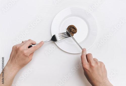 Two female hands hold a stainless steel knife and fork near the plate and cut artificial feces. Fake news, jokes. Concept of inept chef, lousy restaurant, bad food, crappy taste. photo